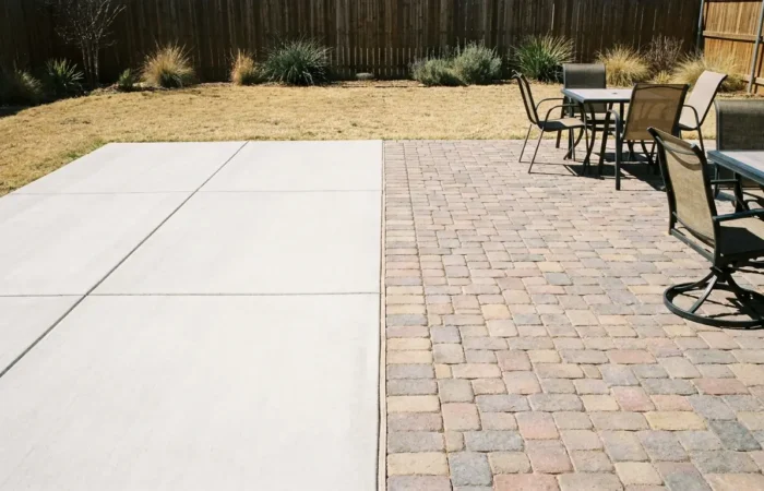 Side-by-side comparison of a poured concrete patio and a paver patio in a Lubbock backyard — concrete vs pavers